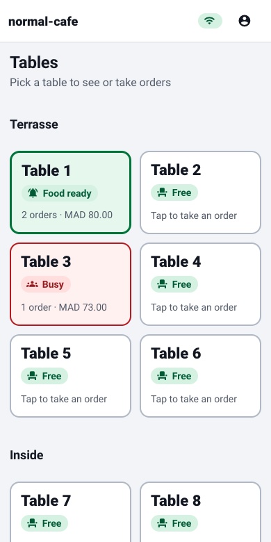 The waiter’s phone showing tables: Table 1 green with Food ready, Table 3 red with Busy and MAD 73.00, and the other tables marked Free.